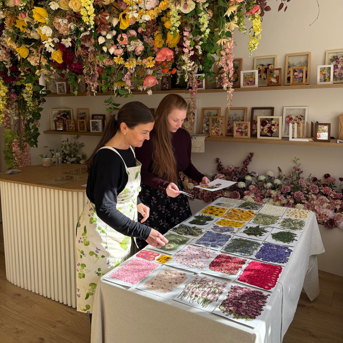 Dvě účastnice workshopu vybírají lisované květiny z roztříděných tácků